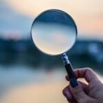 A magnifying glass held by a hand outdoors at sunset, focusing on exploration.